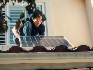 Pracownik instalujący panel fotowoltaiczny na dachu domu, symbolizujący inwestycję w odnawialne źródła energii.