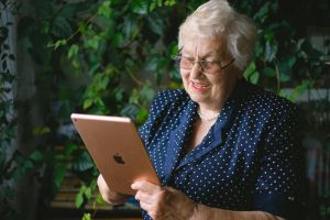 Starsza kobieta z uśmiechem obsługująca tablet w inteligentnym domu, symbolizującą integrację technologii smart home z ogrodnictwem.