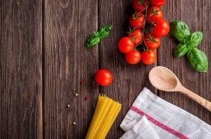 Składniki na makaron: pomidory, bazylia, spaghetti na drewnianym stole.