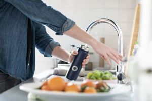 Kobieta sterująca inteligentnym systemem filtracji wody za pomocą smartfona w domu
